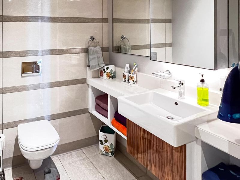 Modern bathroom featuring a wall-mounted toilet, a sleek vanity with a rectangular basin, and large-format wall tiles with decorative horizontal banding.