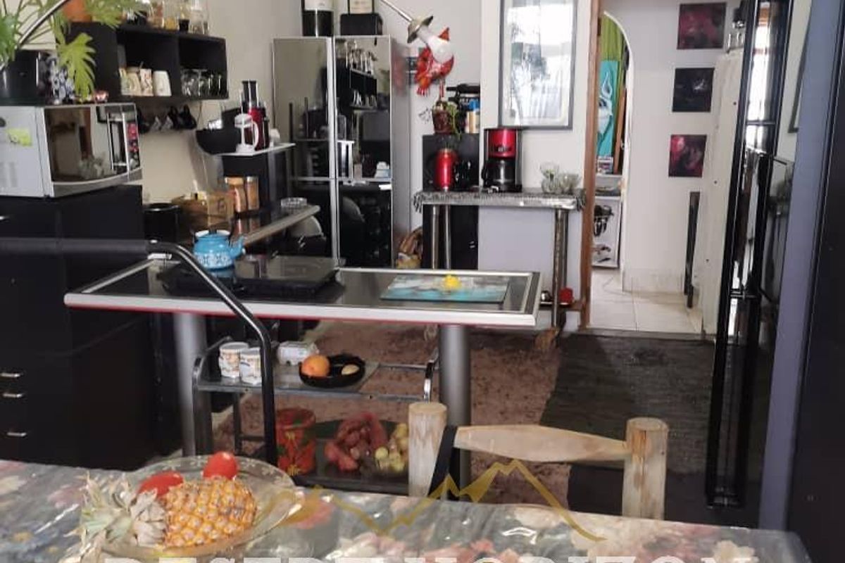 A functional kitchen area featuring tiled flooring and built-in shelving, currently utilized with various appliances and storage solutions.