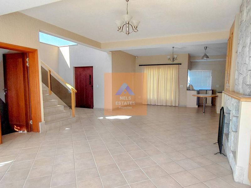 Spacious open-plan living area featuring tiled floors, a stone-clad fireplace, and a staircase, offering a versatile layout for dining and lounge arrangements.