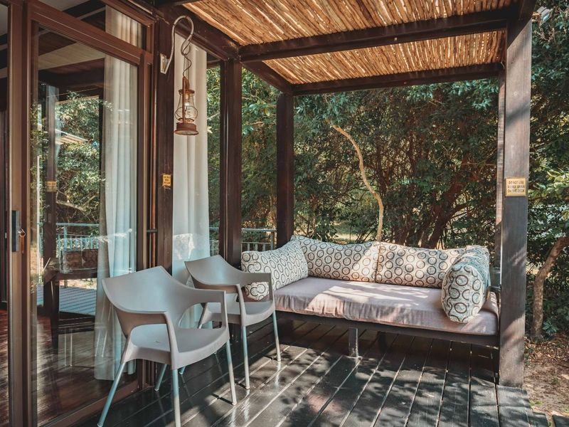 A covered outdoor patio featuring timber decking, a thatched roof, and sliding glass doors providing seamless access to the interior living space.