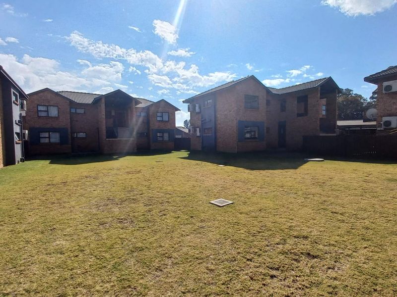 A view of the rear exterior of the townhouse complex, featuring brick buildings, a shared lawn area, and perimeter fencing.