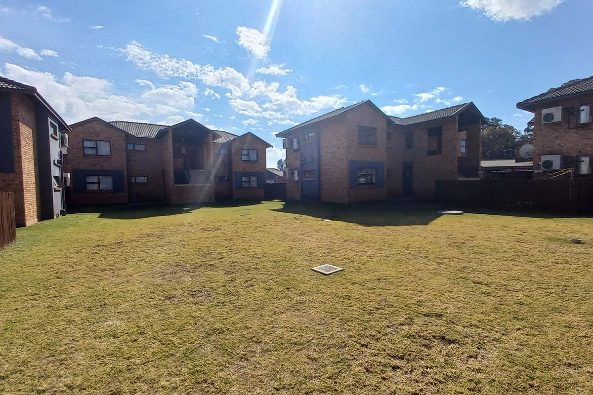 A view of the rear exterior of the townhouse complex, featuring brick buildings, a shared lawn area, and perimeter fencing.