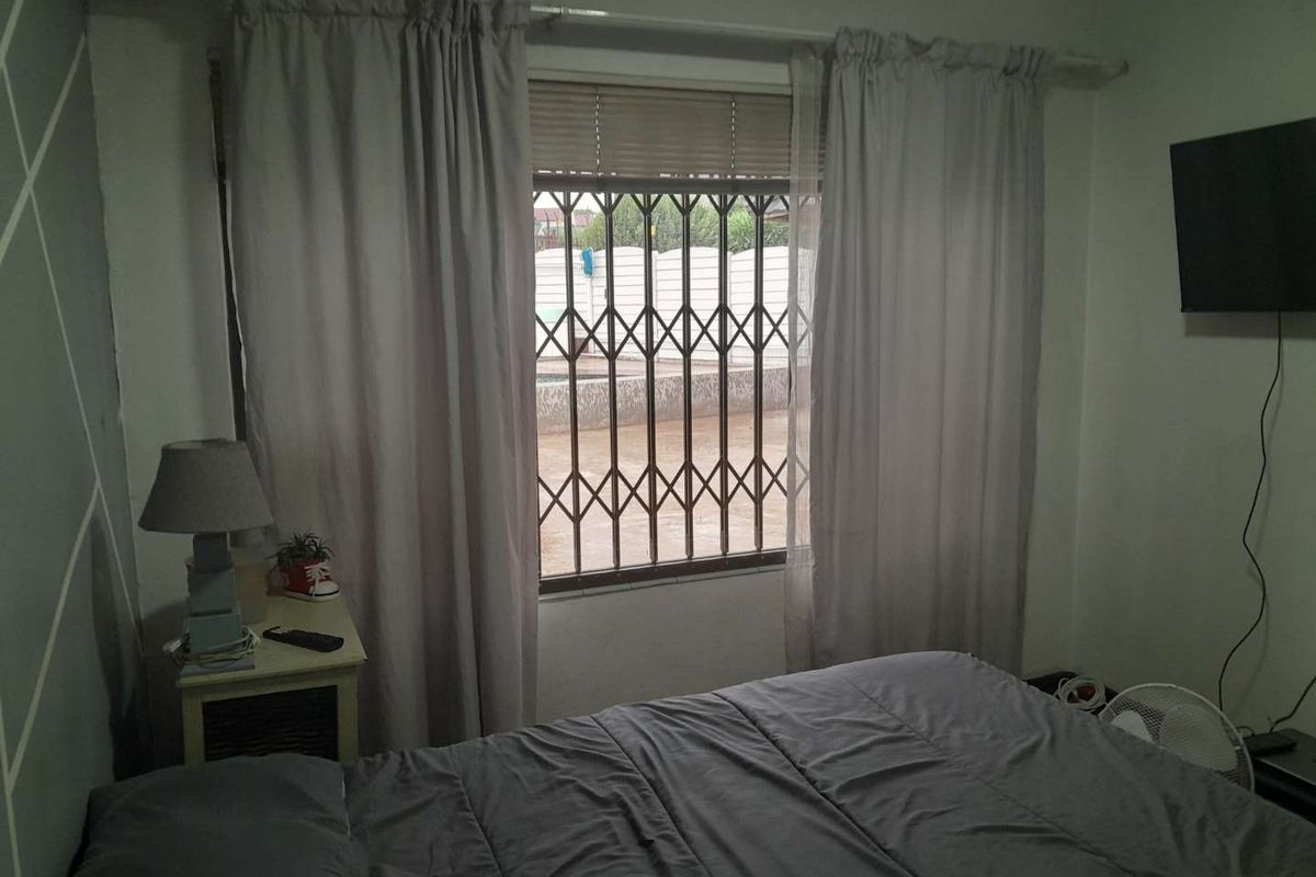 A bedroom featuring a window with a fitted security gate and curtain rail, providing a view of the exterior area.