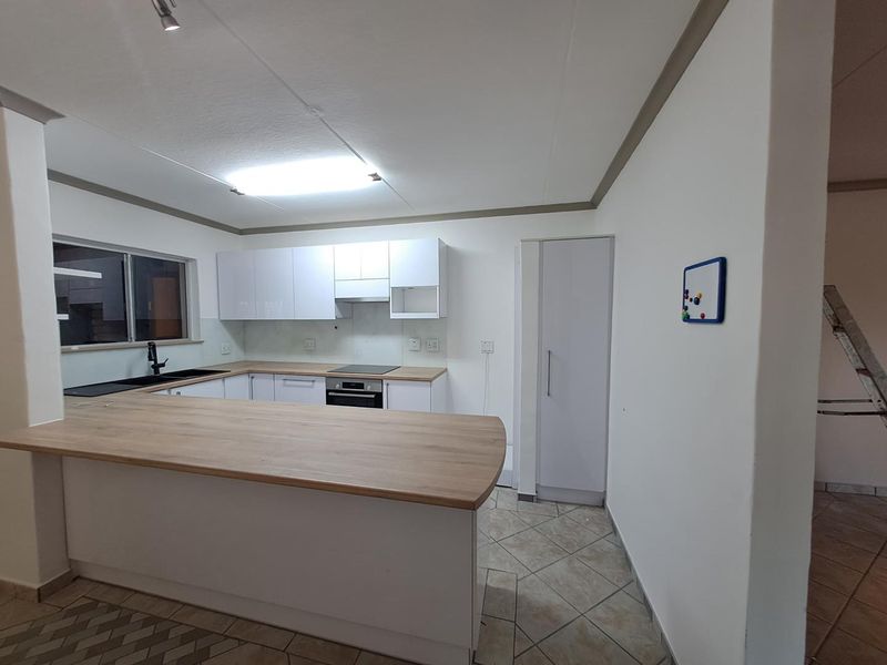 Modern kitchen featuring white cabinetry, wood-look laminate countertops, a breakfast bar, and integrated appliances, set against neutral tiled flooring.