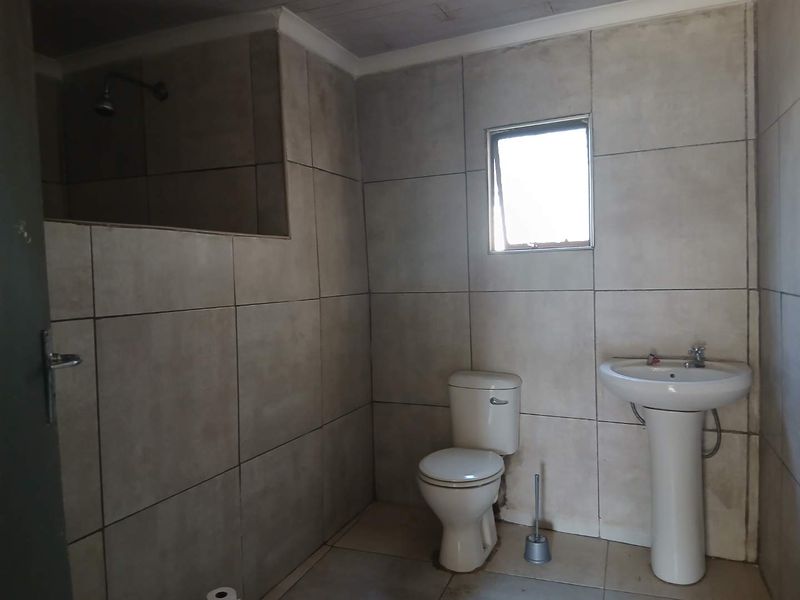 A functional bathroom featuring a pedestal basin, toilet, and a tiled shower enclosure with neutral wall and floor tiling.