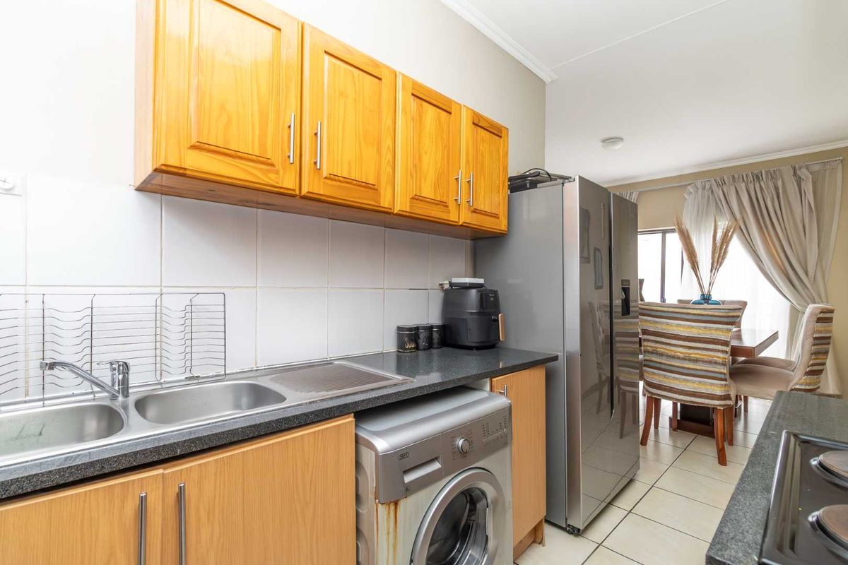 A functional kitchen area featuring wooden cabinetry, a double stainless steel sink, tiled splashbacks, and space for a washing machine.