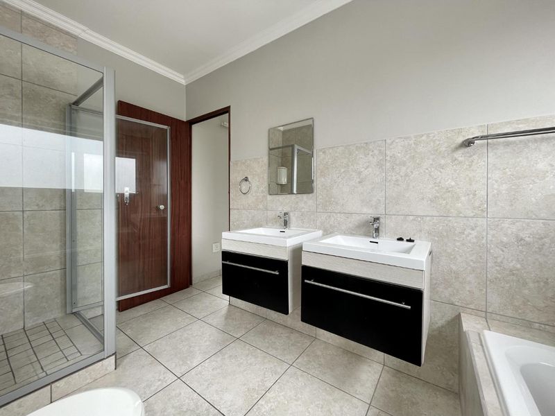 Modern bathroom featuring a double vanity, glass-enclosed shower, and a built-in bathtub with neutral floor-to-ceiling tiling.