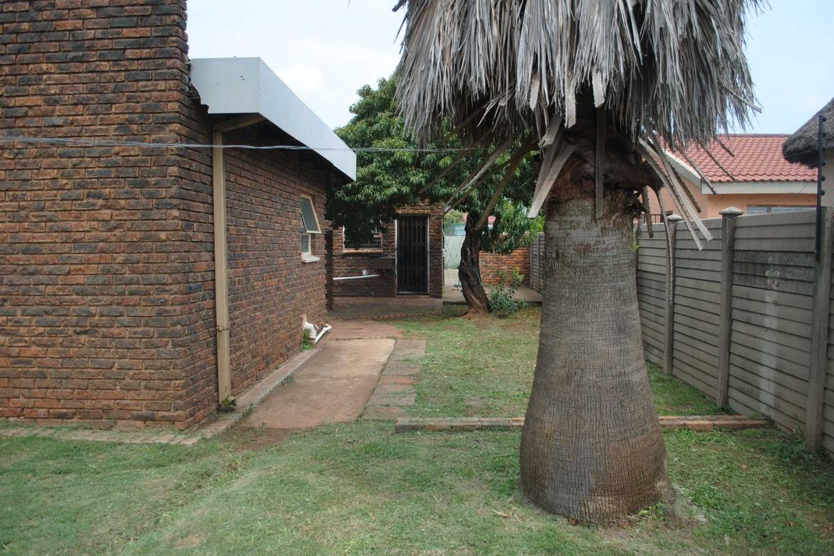 A view of the rear garden area featuring face-brick exterior walls, a concrete boundary fence, and established garden landscaping.