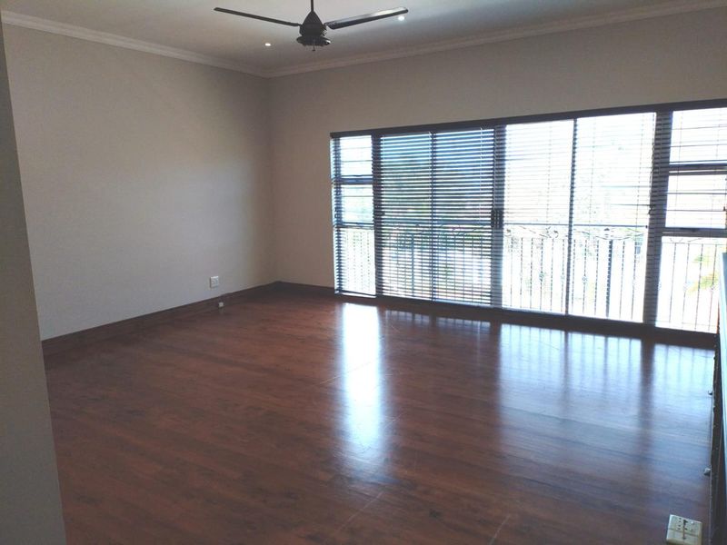 Spacious, empty bedroom featuring dark laminate flooring, a ceiling fan, recessed lighting, and large sliding glass doors with security bars and venetian blinds.