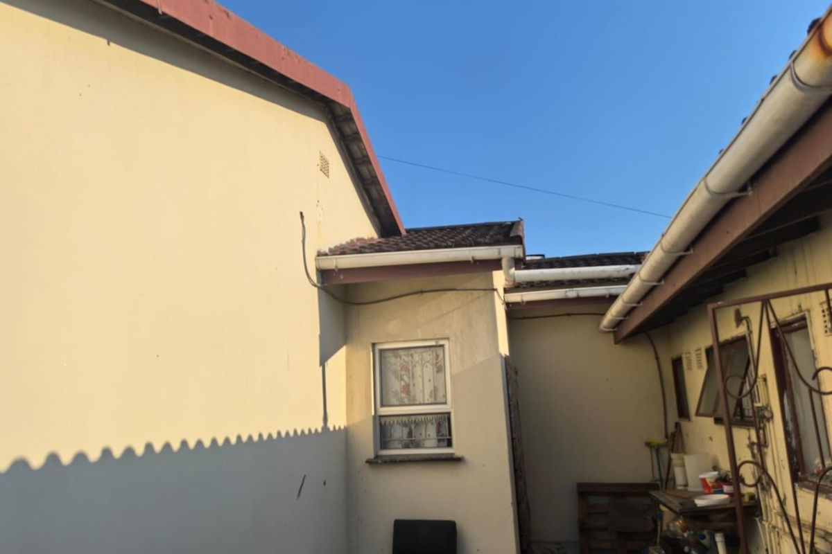 A view of the rear exterior building facade showing tiled roofing, guttering, and window fixtures in need of maintenance.