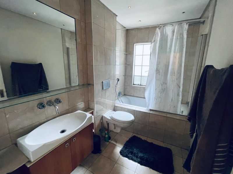 A functional bathroom featuring a wall-mounted toilet, built-in bathtub with shower, vanity cabinet with basin, and neutral wall tiling.