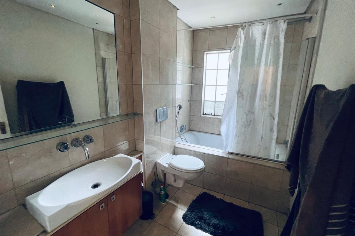 A functional bathroom featuring a wall-mounted toilet, built-in bathtub with shower, vanity cabinet with basin, and neutral wall tiling.