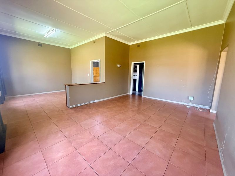 Spacious open-plan living area featuring tiled flooring and a central partition wall, offering a blank canvas for renovation and interior design.