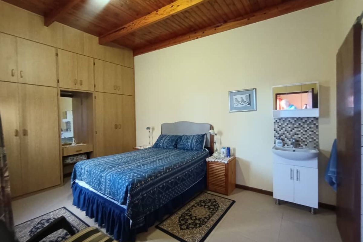 Bedroom featuring a high timber-beamed ceiling, extensive built-in wooden cabinetry, and a vanity basin with mosaic tile splashback.