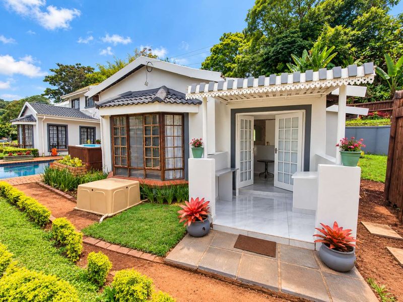 A well-maintained rear exterior view featuring a tiled patio with a pergola, french doors, and access to a swimming pool area.