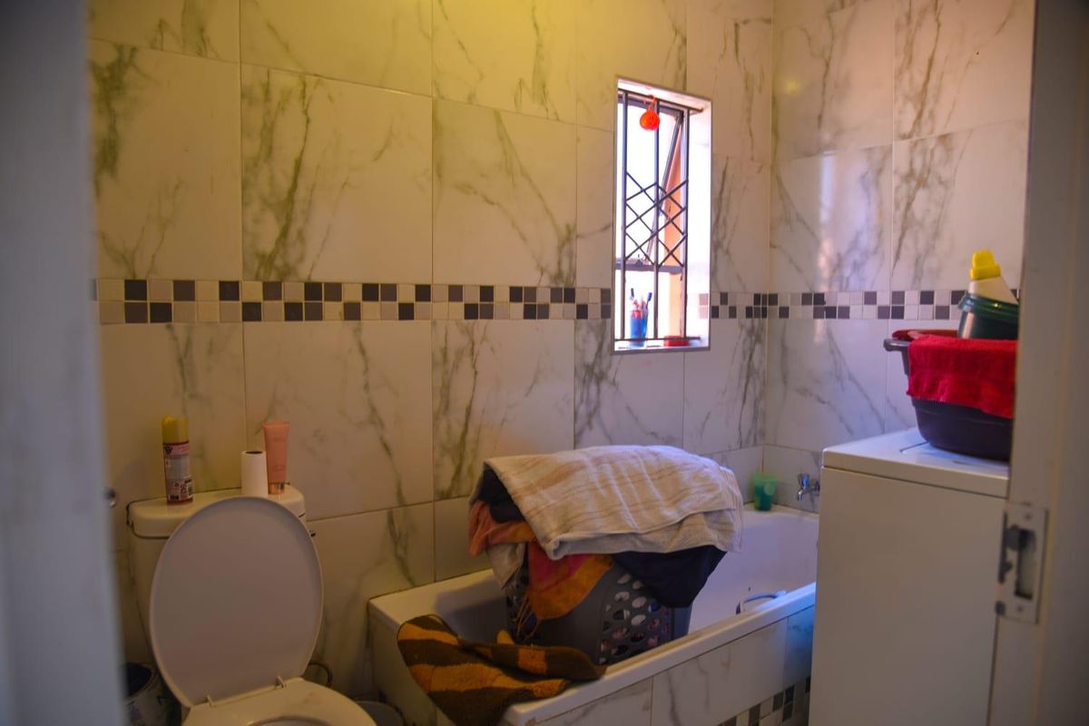 A functional bathroom featuring marble-effect wall tiles, a standard bathtub, and a toilet, providing essential sanitary facilities.