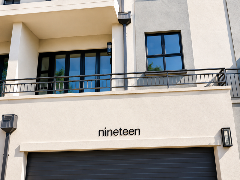 Modern exterior facade featuring a garage door, balcony with metal railing, and contemporary wall lighting.