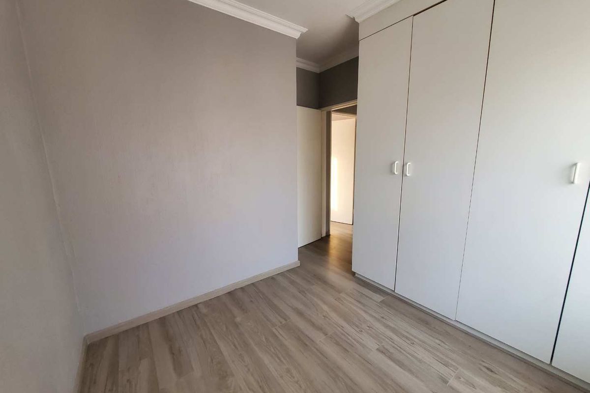 A bright, empty bedroom featuring modern laminate flooring, neutral wall tones, and ample built-in cupboard storage space.