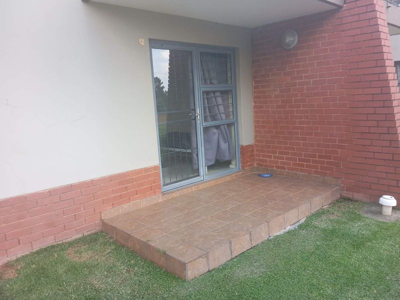 A ground floor tiled patio area featuring a brick facade and an aluminium sliding door with security gate access.