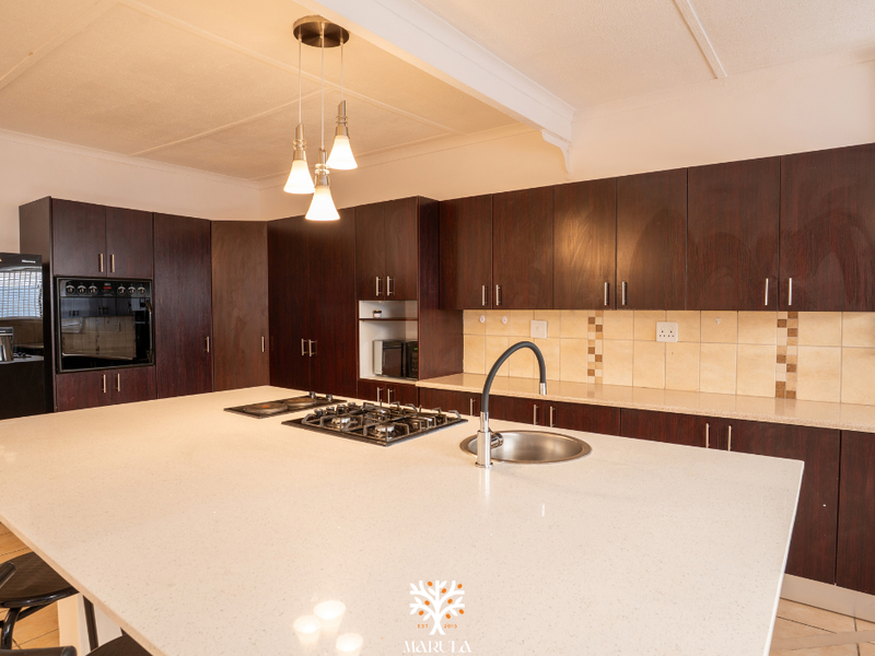 Spacious kitchen featuring dark wood cabinetry, a large central island with a gas hob and sink, and stone countertops.
