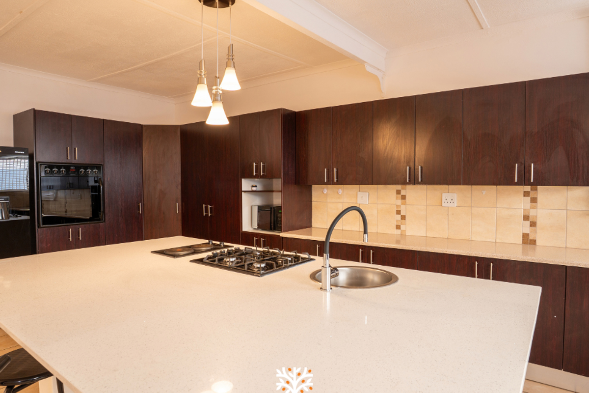 Spacious kitchen featuring dark wood cabinetry, a large central island with a gas hob and sink, and stone countertops.