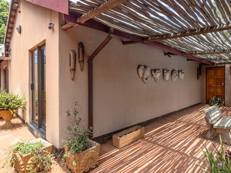 A covered outdoor patio area featuring a rustic thatched pergola, terracotta tiling, and direct access to the home through sliding glass doors.