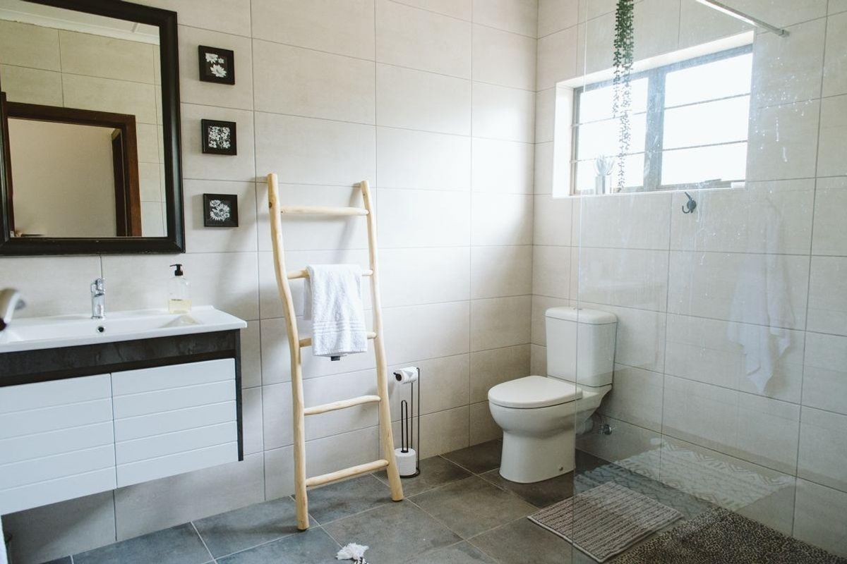 A modern bathroom featuring a vanity cabinet, ceramic basin, toilet, and a glass-enclosed shower with neutral wall and floor tiling.