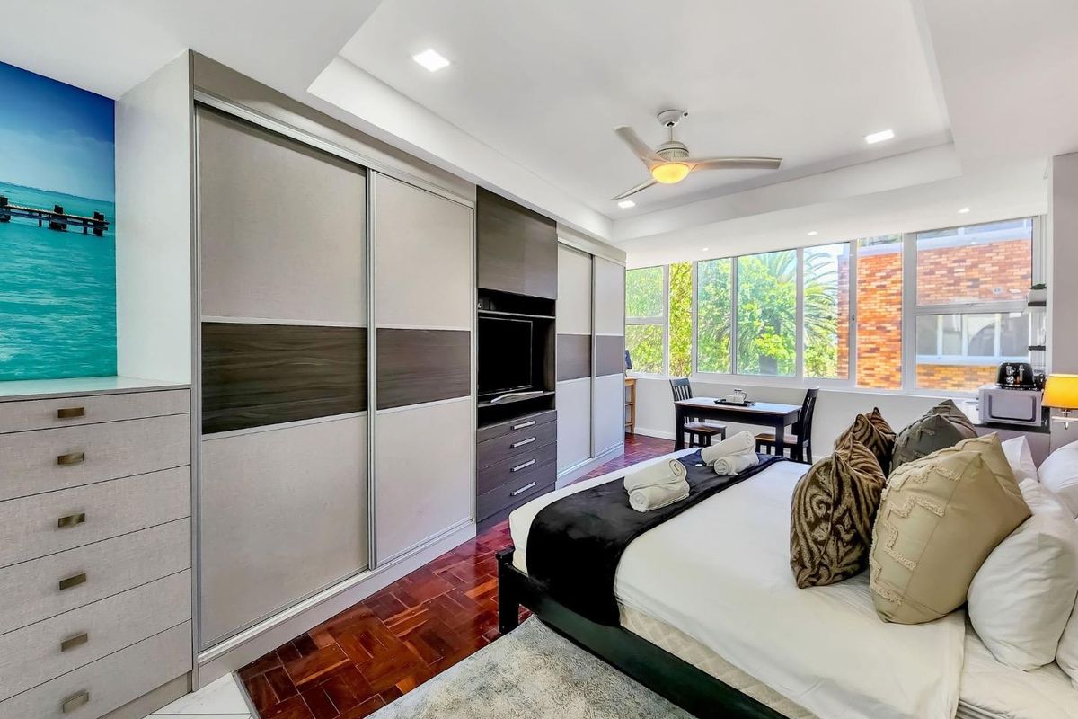 Spacious bedroom featuring polished parquet flooring, extensive built-in cabinetry with integrated storage, recessed ceiling lighting, and large windows providing natural light.