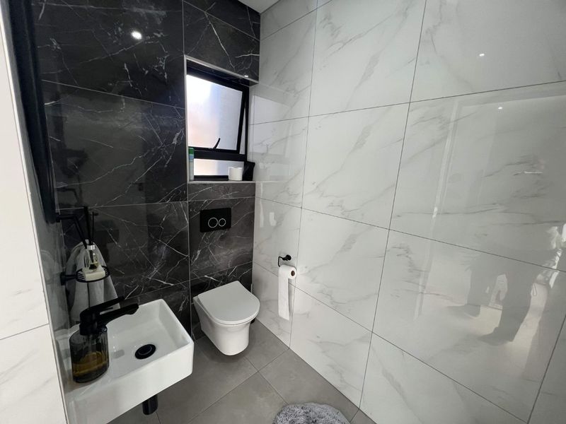 Modern guest bathroom featuring high-contrast black and white marble-look porcelain tiling, a wall-mounted toilet with concealed cistern, and a sleek wall-mounted basin.