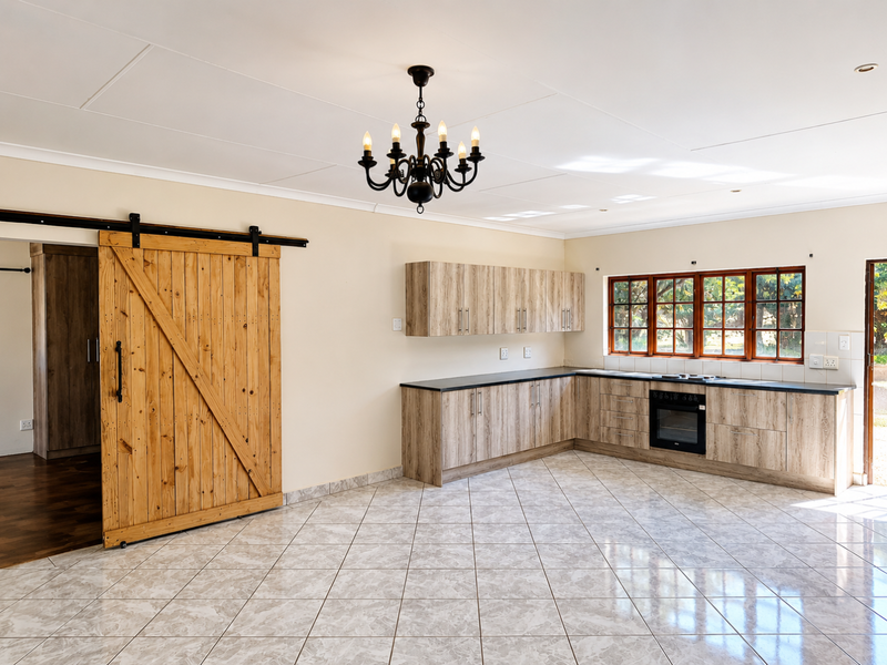 Spacious kitchen featuring light wood-finish cabinetry, dark countertops, built-in oven and hob, tiled flooring, and a distinctive sliding barn door.