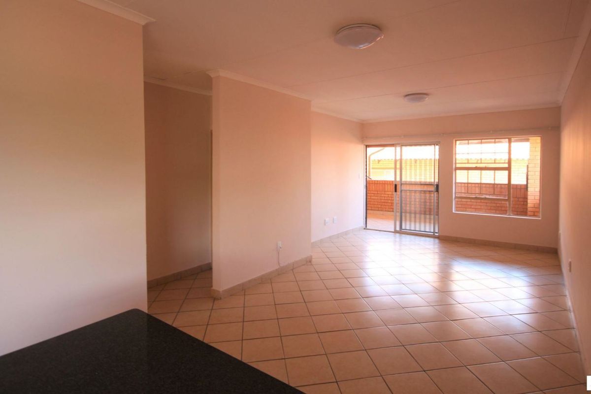 A spacious, empty living area featuring tiled floors, neutral walls, and a sliding glass door providing access to an outdoor balcony.