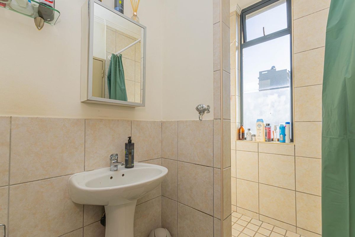 A functional bathroom featuring a pedestal basin, mirrored medicine cabinet, and a tiled shower area with a window for natural light.