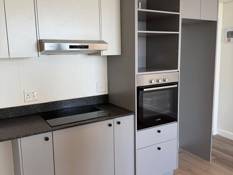 Modern kitchen featuring sleek grey and white cabinetry, stone countertops, integrated oven, electric hob, and high-quality laminate flooring in a clean, contemporary space.