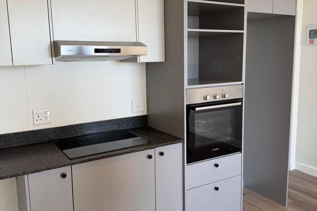 Modern kitchen featuring sleek grey and white cabinetry, stone countertops, integrated oven, electric hob, and high-quality laminate flooring in a clean, contemporary space.