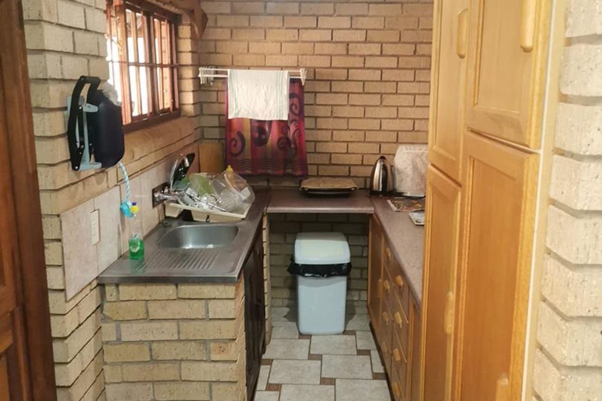 Compact kitchen featuring exposed brick walls, tiled flooring, built-in wooden cabinetry, and a stainless steel sink under a traditional thatched roof.