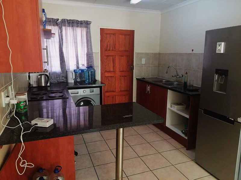 A functional kitchen featuring granite countertops, built-in wooden cabinetry, a double basin sink, and tiled flooring, with a dedicated space for laundry appliances.