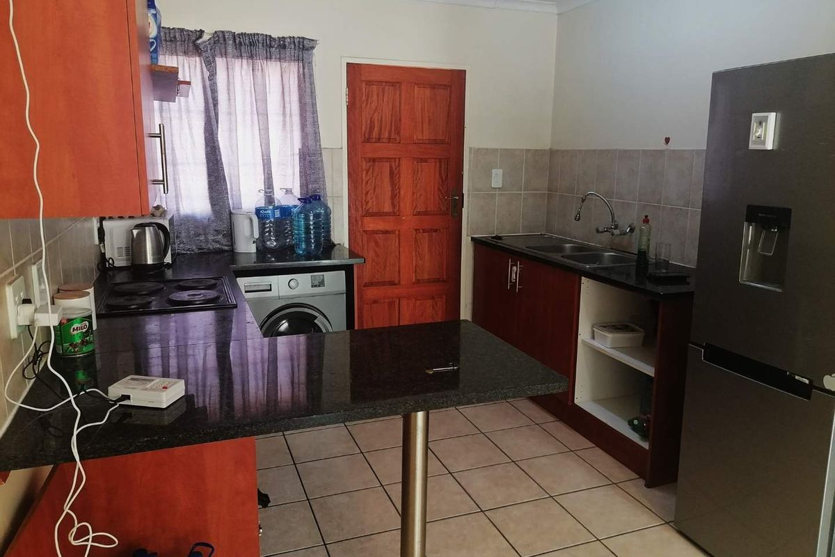 A functional kitchen featuring granite countertops, built-in wooden cabinetry, a double basin sink, and tiled flooring, with a dedicated space for laundry appliances.