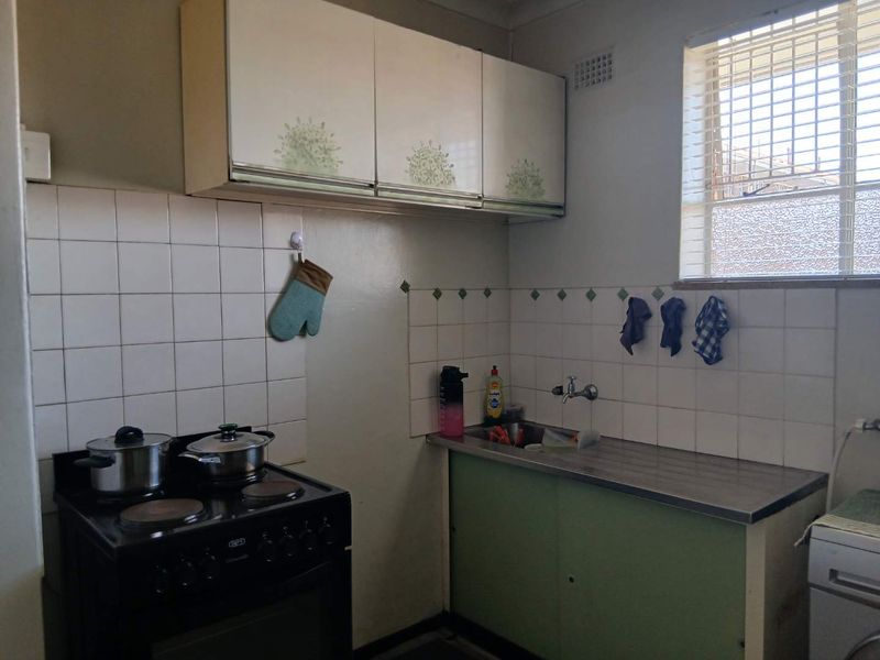 A compact, dated kitchen featuring original cabinetry, a stainless steel sink, tiled backsplash, and a freestanding stove, offering potential for modernization.