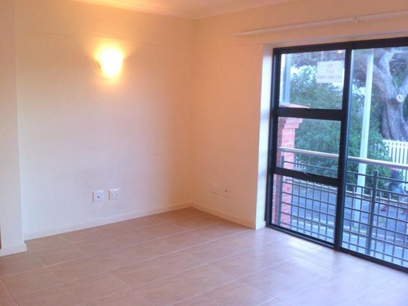 An empty living room featuring tiled flooring, a wall-mounted light fixture, and a large sliding glass door providing access to an outdoor area.