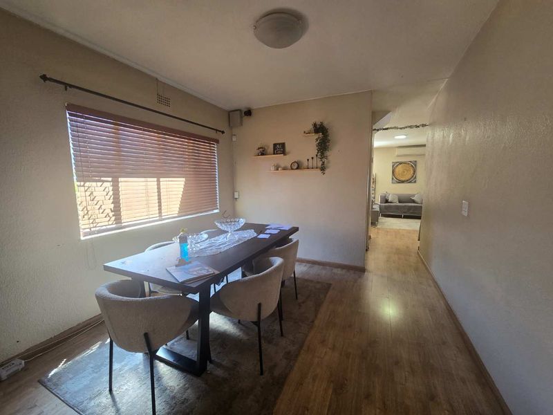 Dining area featuring laminate flooring, venetian blinds, and neutral wall finishes, providing a functional space with direct access to the adjacent living area.
