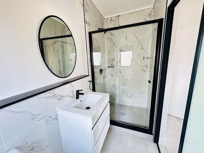 Modern bathroom featuring a sleek vanity with black fixtures, marble-look wall tiling, and a contemporary glass shower enclosure with a black frame.