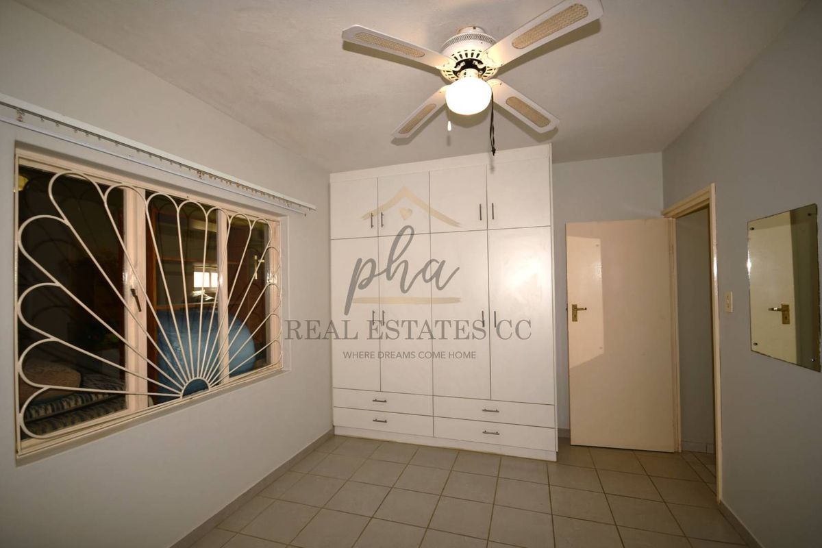 A bedroom featuring built-in cabinetry, tiled flooring, a ceiling fan, and security bars on the window.