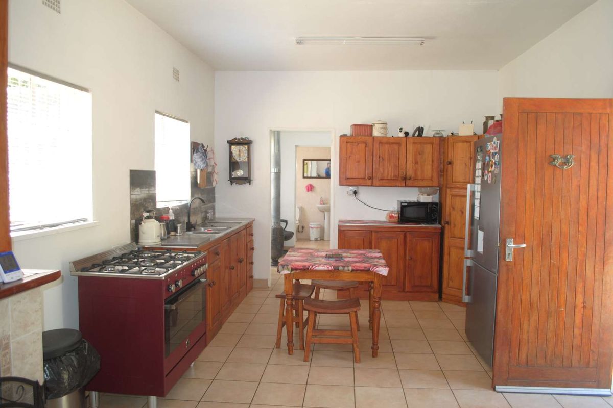 A functional kitchen featuring wooden cabinetry, a gas stove, and tiled flooring, with an adjacent view into a bathroom area.