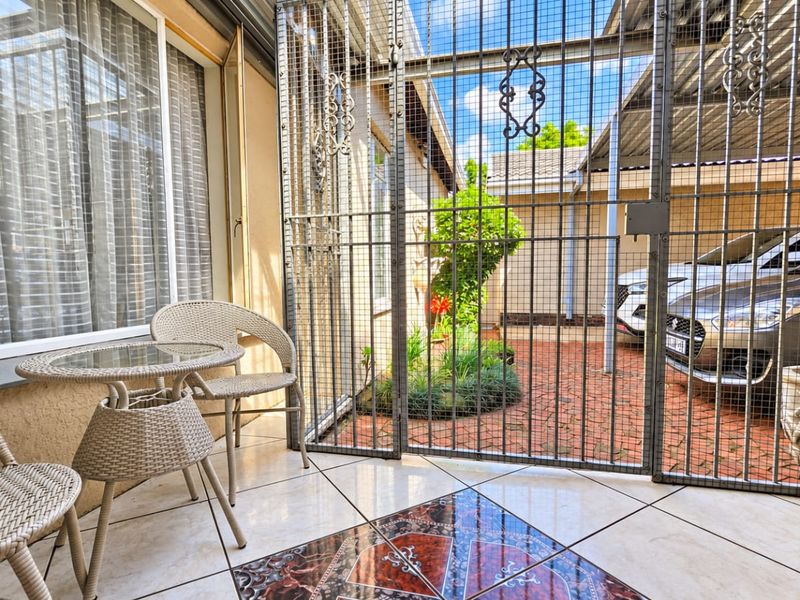 A covered patio area featuring tiled flooring and a secure metal gate, providing access to a paved courtyard and driveway area.