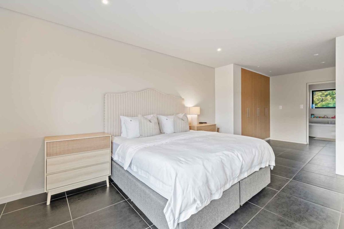 Spacious bedroom featuring modern tiled flooring, recessed downlighting, and integrated built-in cupboards, with an en-suite bathroom visible in the background.