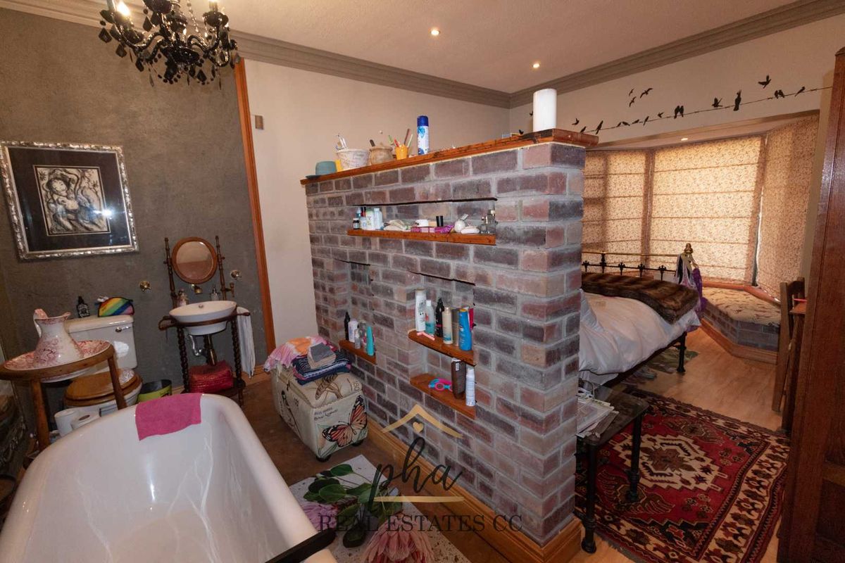 A unique open-plan bedroom featuring a central exposed brick partition wall that separates the sleeping area from a freestanding bathtub and vanity.