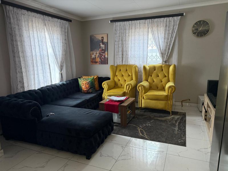 A well-maintained living room featuring polished tiled flooring and dual window treatments with curtain rails.