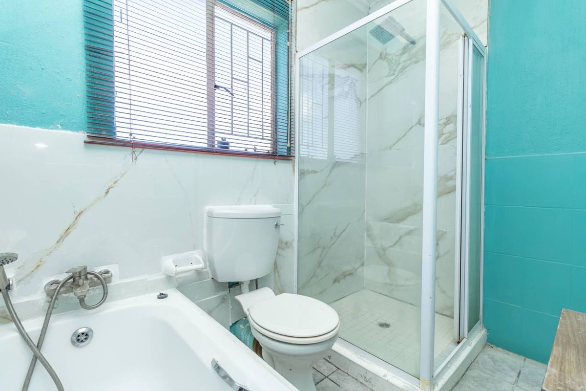 A functional bathroom featuring a white bathtub, a separate glass-enclosed shower, and a toilet, finished with marble-look wall tiles and vibrant blue accents.