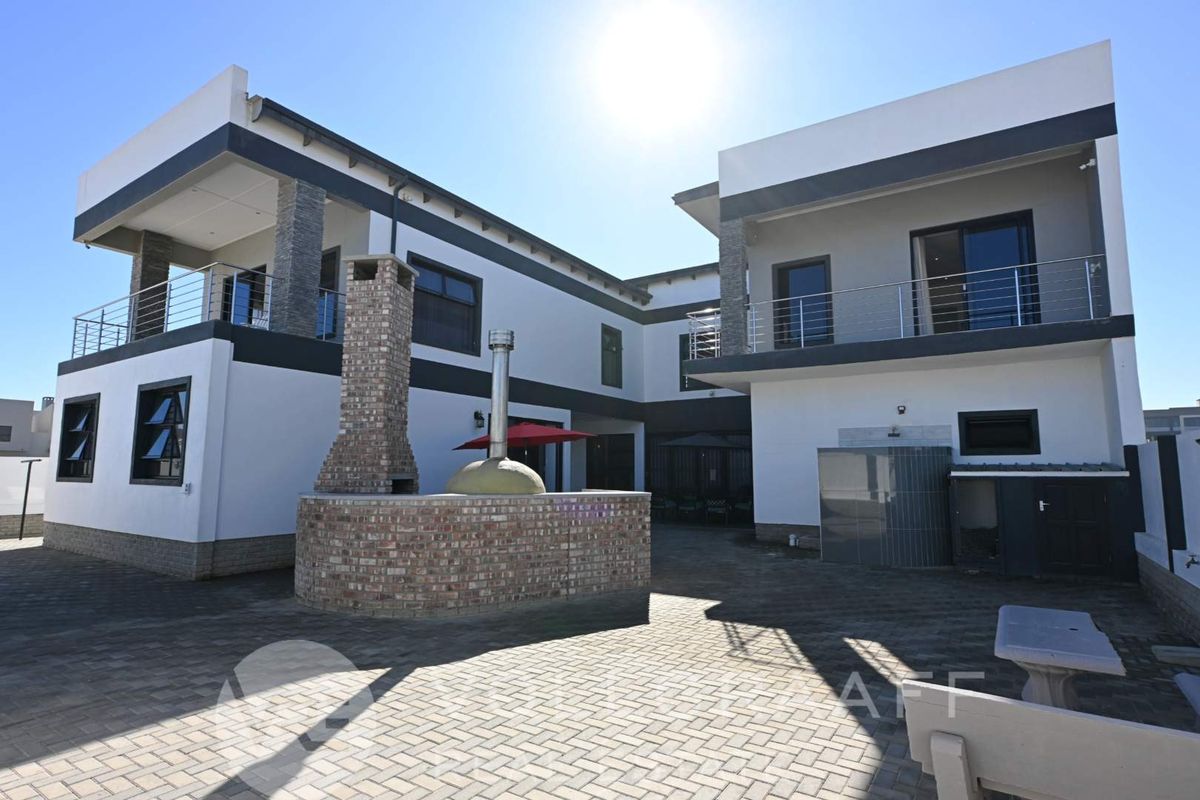 Spacious rear courtyard featuring a built-in brick fireplace and pizza oven, surrounded by a modern two-story home with balconies and paved outdoor area.