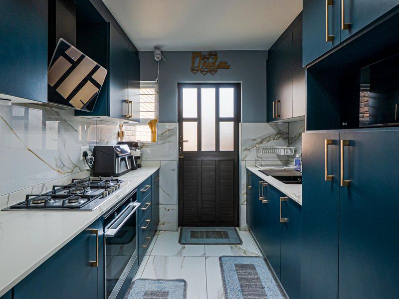 Modern galley kitchen featuring dark blue cabinetry, marble-look splashbacks, quartz countertops, gas hob, and built-in oven with direct access to the exterior.